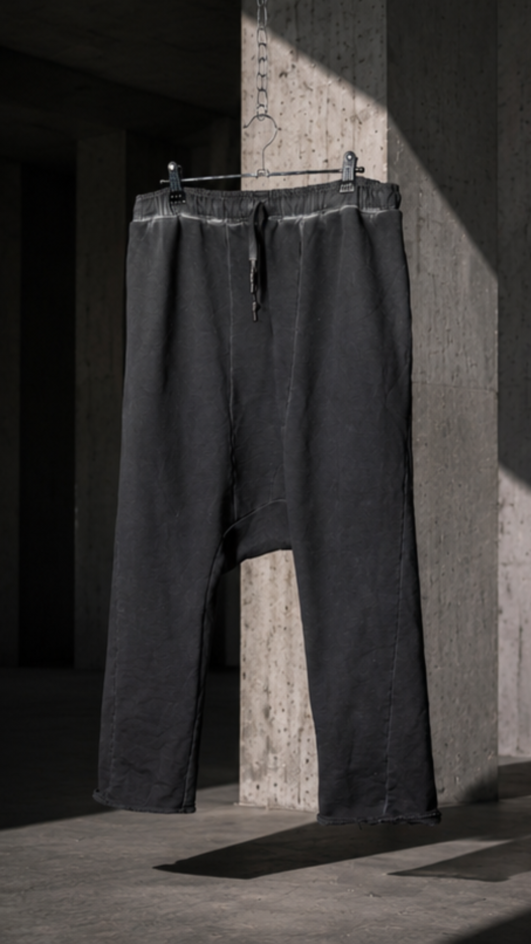 Black pants hanging on a rack against a concrete wall.