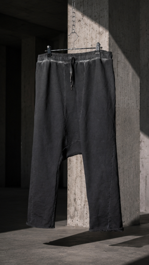 Black pants hanging on a rack against a concrete wall.